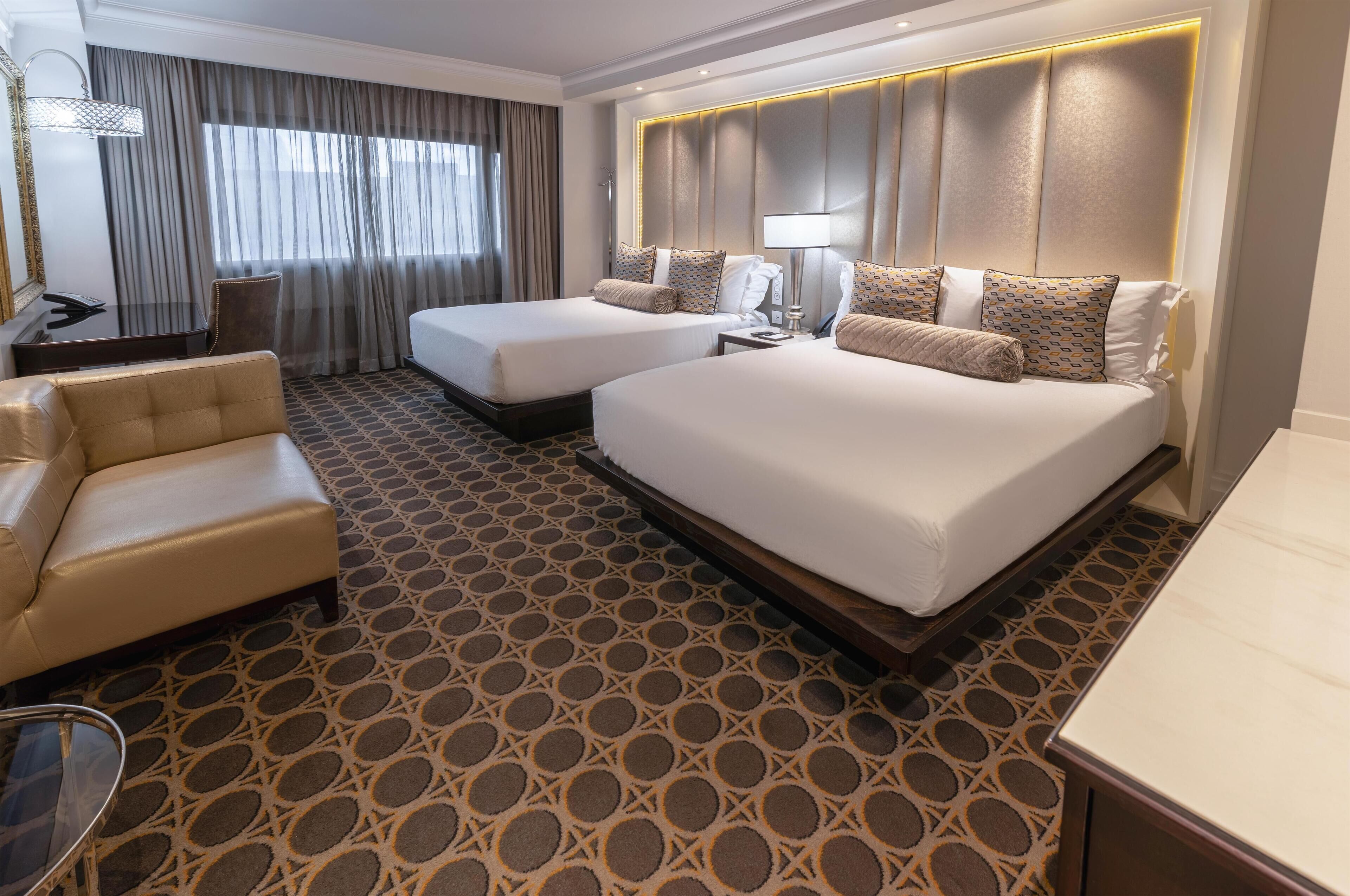 A hotel room with two beds, a desk, a chair, and a patterned carpet.
