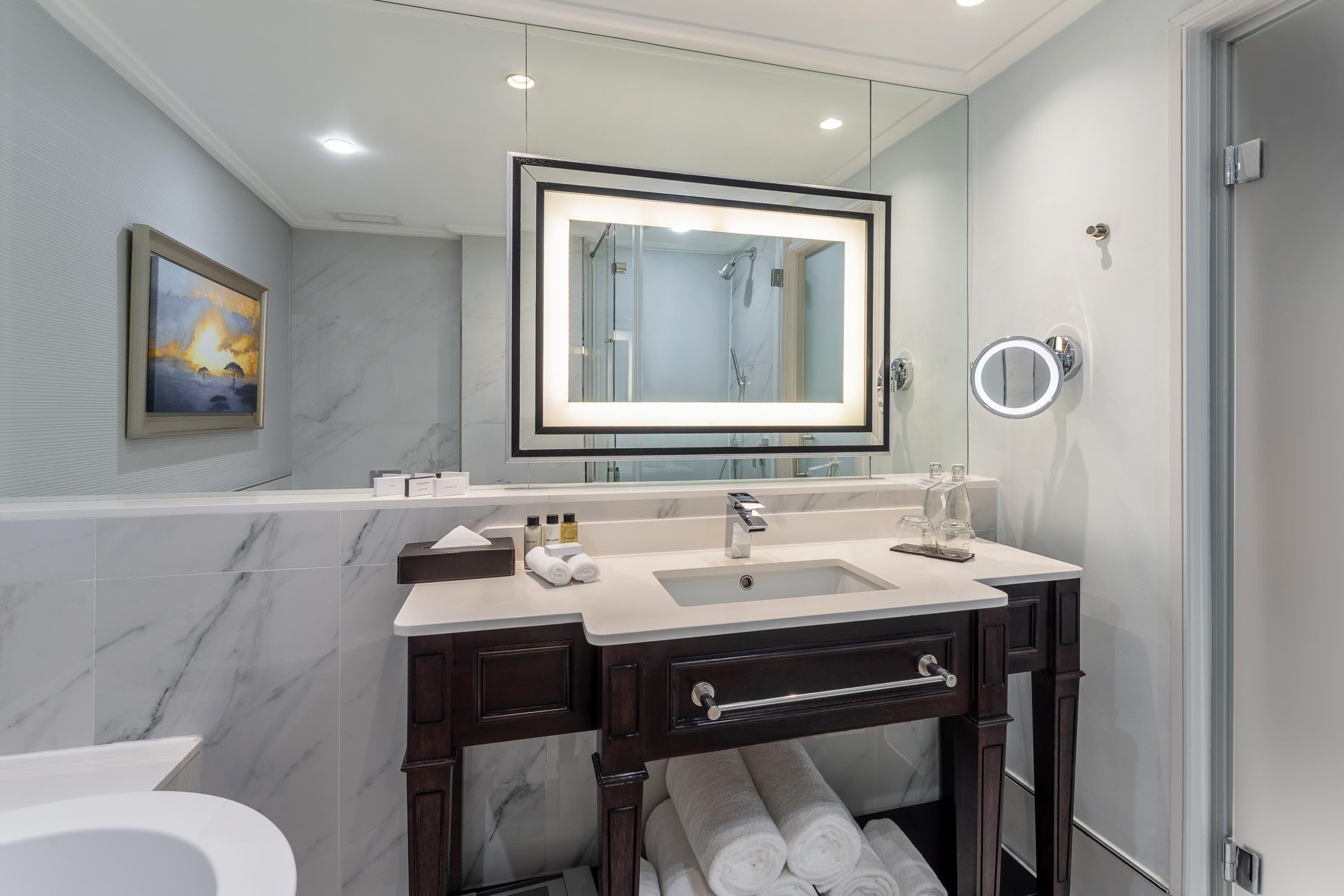 A modern bathroom with a marble vanity, a large mirror, a glass shower enclosure, and a toilet.