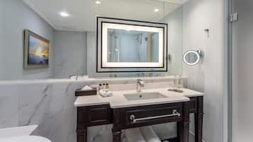A modern bathroom with a marble vanity, a large mirror, a glass shower enclosure, and a toilet.