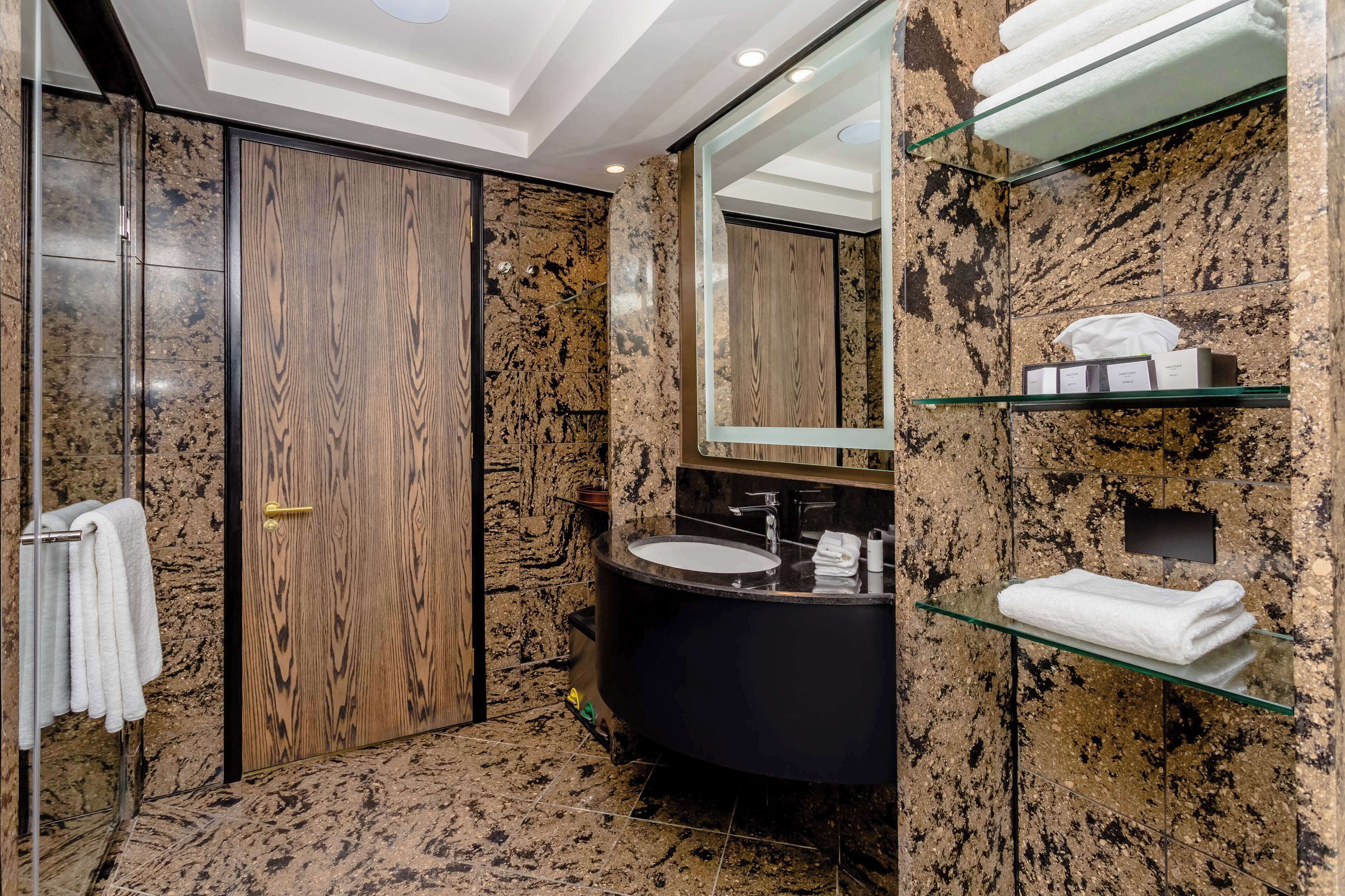 A modern bathroom with a wooden door, a black sink, and marble walls.