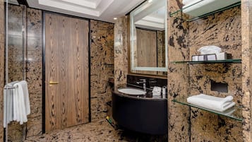 A modern bathroom with a wooden door, a black sink, and marble walls.