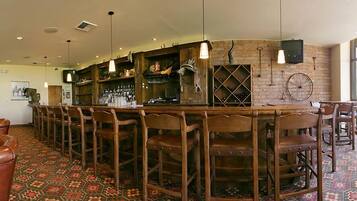 Una zona de bar con sillas de madera, una barra y una pared de ladrillo con botelleros.