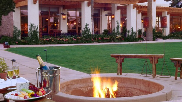 Eine Terrasse im Freien mit Feuerstelle, einem Tisch mit Getränken und einem Gebäude im Hintergrund.