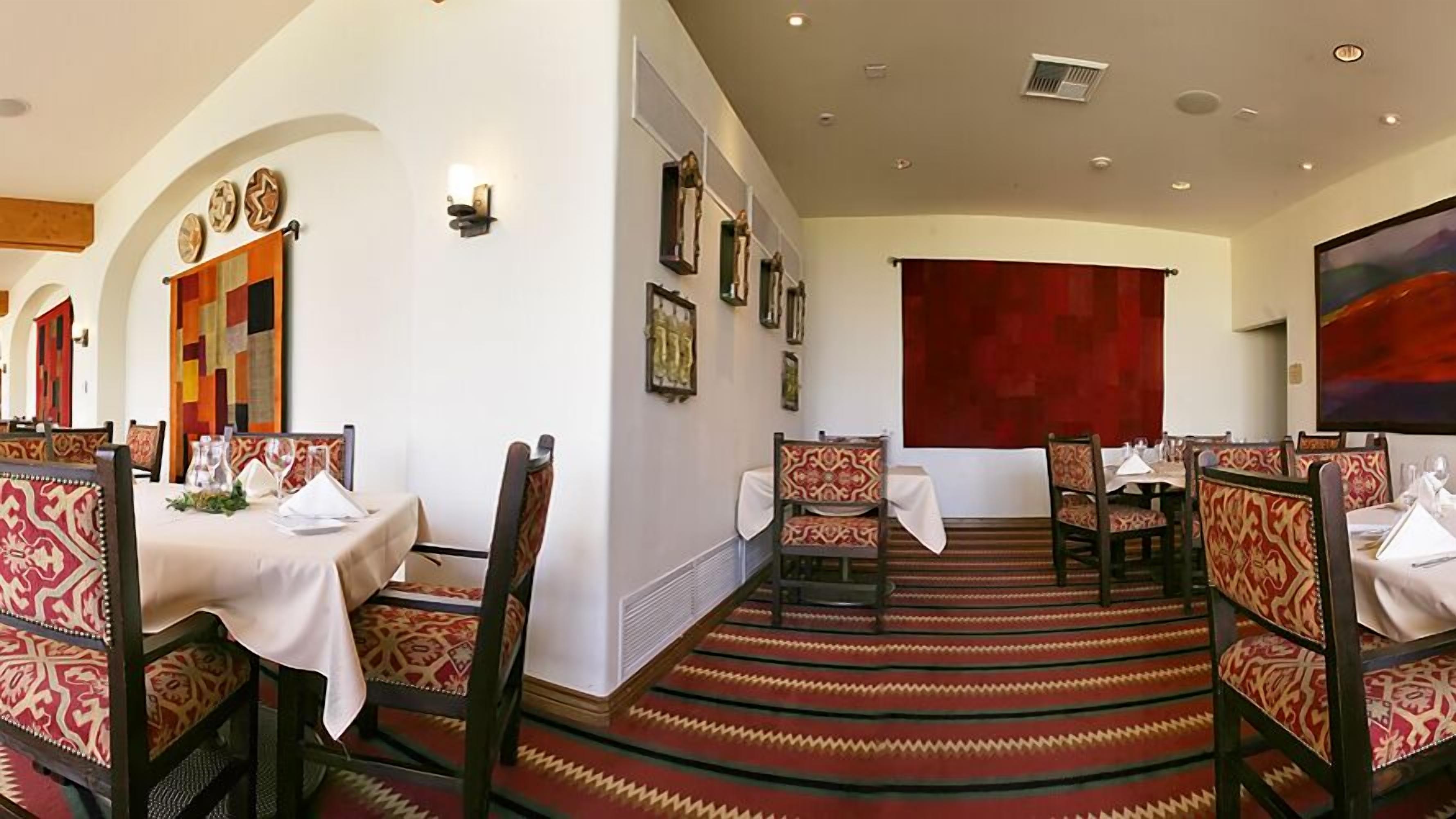 A dining area with tables set for two, chairs with patterned upholstery, and a red carpeted floor.