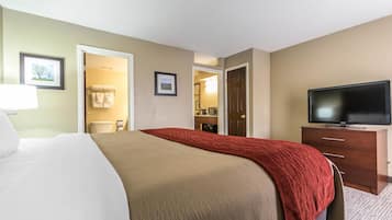A hotel room with a bed, a television, a dresser, and a bathroom visible through an open door.