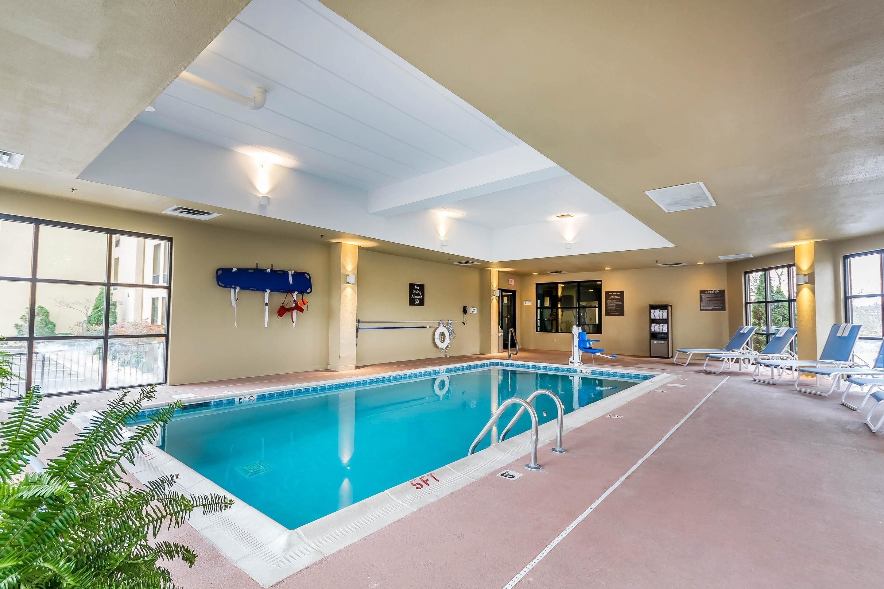 Una piscina interior con carriles claramente delimitados, una silla de salvavidas y sillones de descanso.