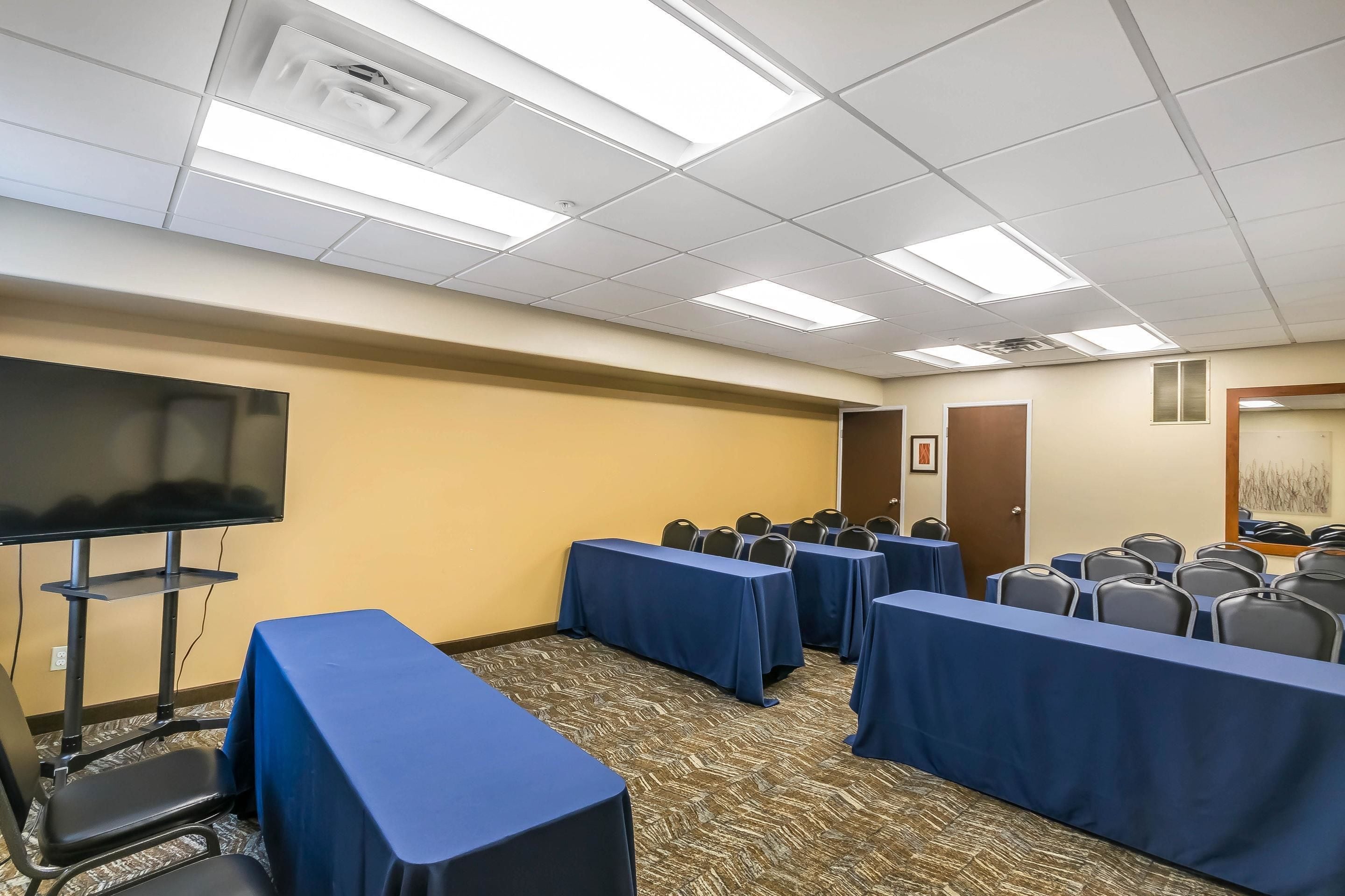 A conference room with tables covered in blue tablecloths, a flat-screen TV, and rows of chairs.