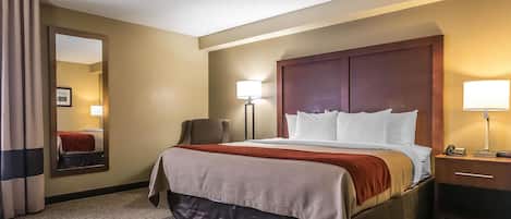 A hotel room with a large bed, a desk, a chair, a mirror, and two bedside lamps.