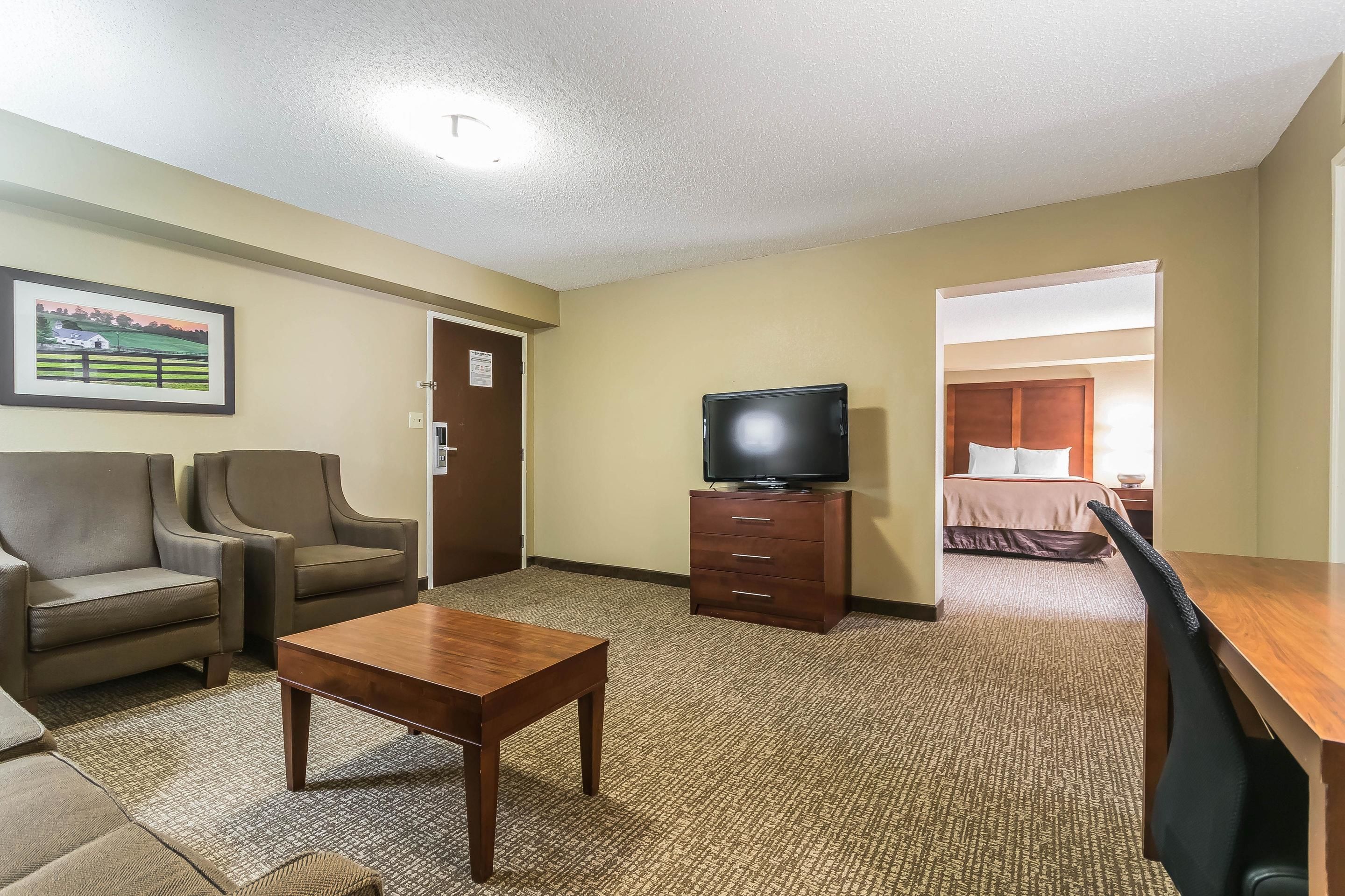 Ein Hotelzimmer mit einer Couch, einem Fernseher auf einem Holztisch, einem Schreibtisch und Teppichboden.