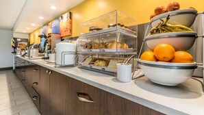 A buffet counter with various food items and a bowl of oranges. - Comfort Inn & Suites Lexington - Hamburg I-75 (Lexington)