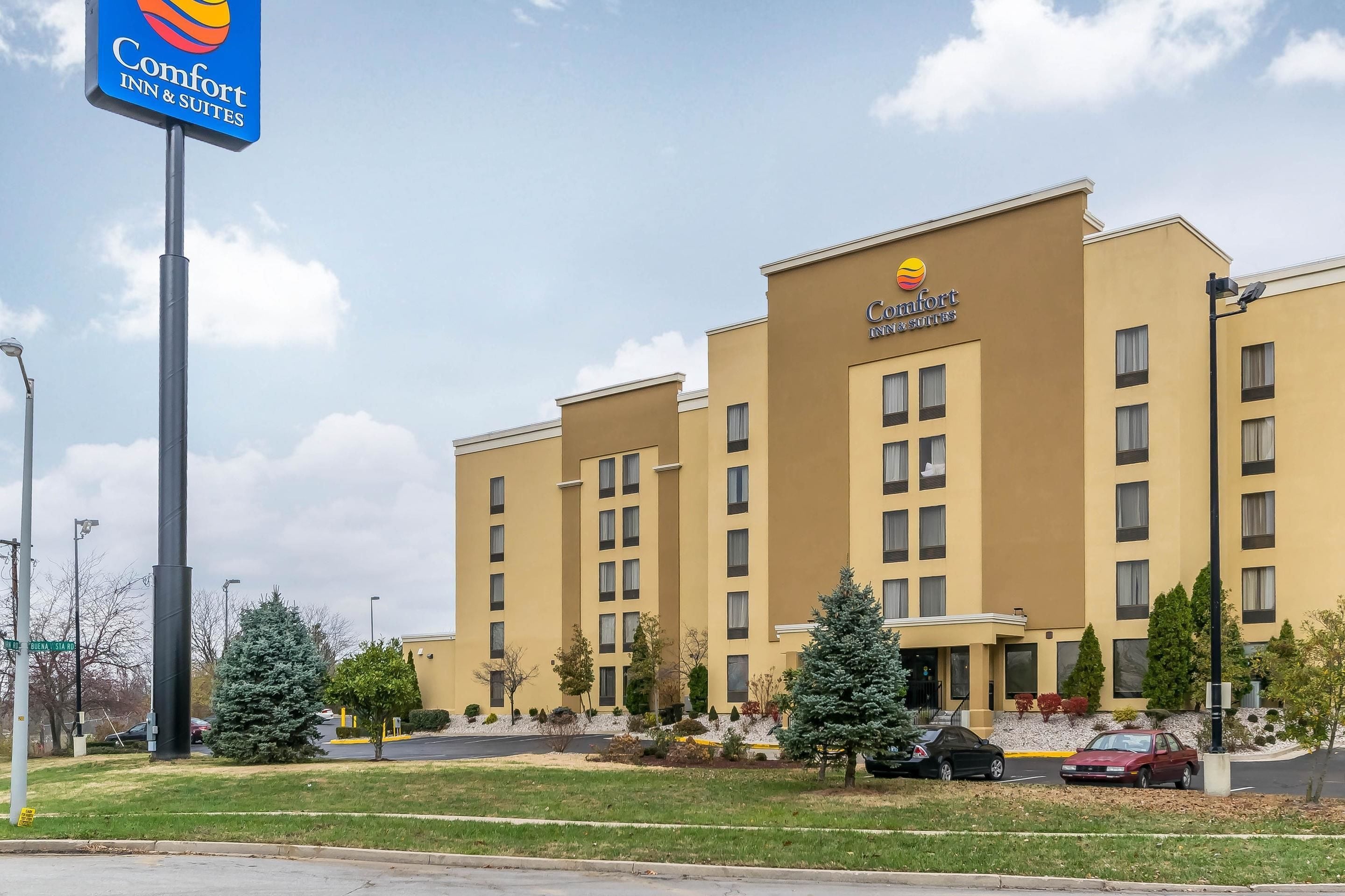 Een Comfort Inn & Suites hotel met een gele gevel, meerdere ramen en een parkeerplaats met auto's.