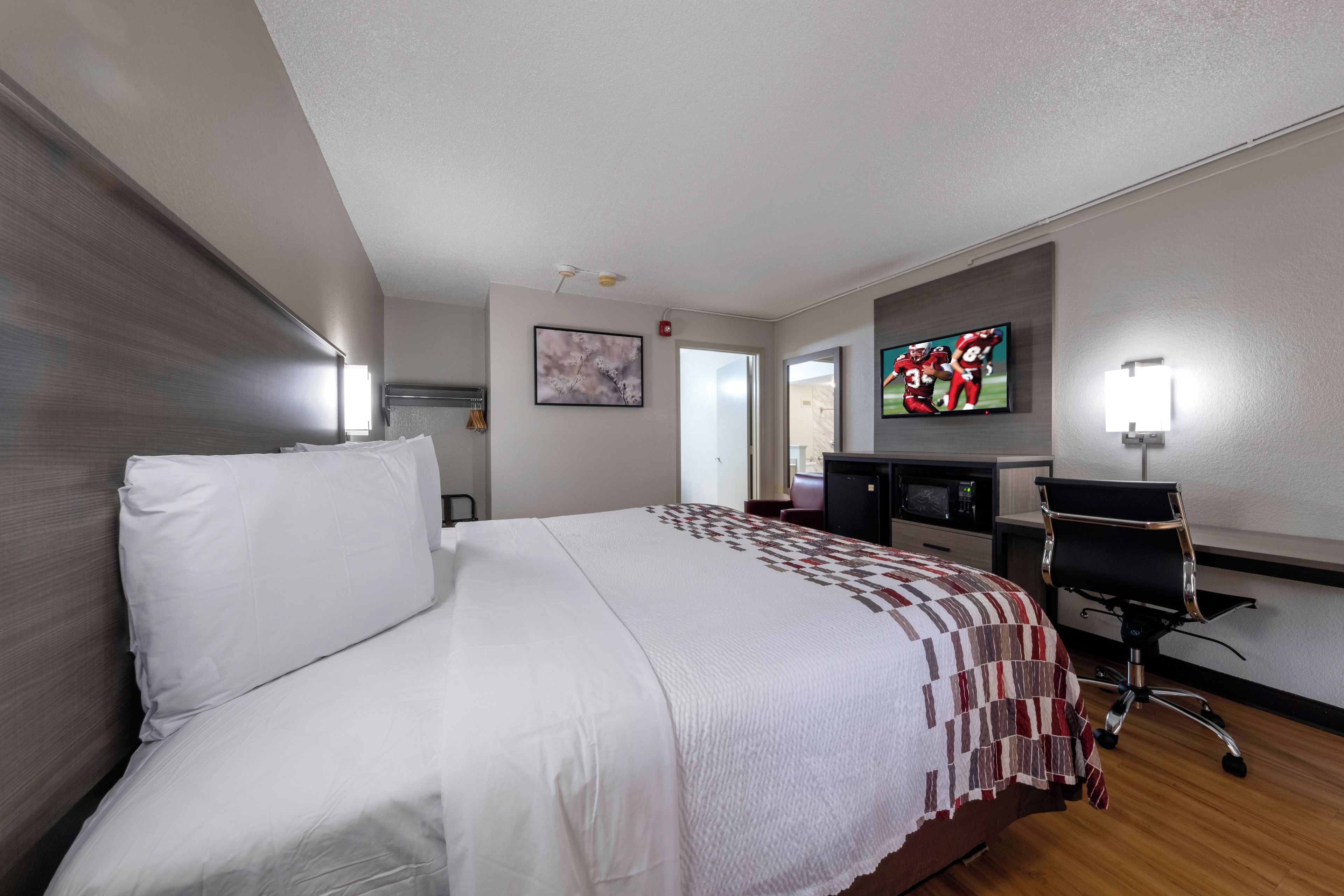 Una habitación de hotel con cama, escritorio, televisión y silla.