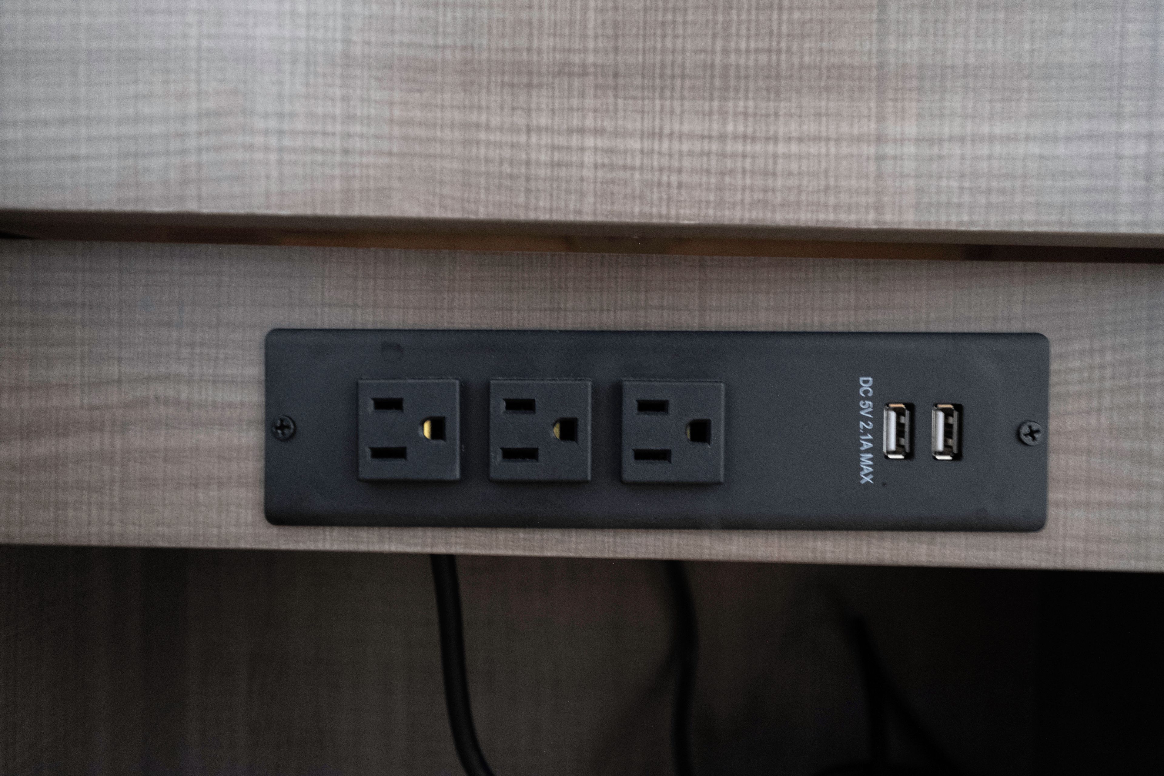 A power strip with three standard electrical outlets and two USB ports, mounted on a textured wall.