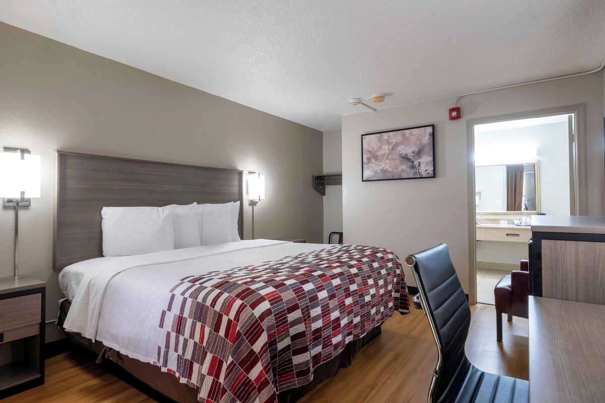Una habitación de hotel con una cama, lámparas de noche, un escritorio y una silla.