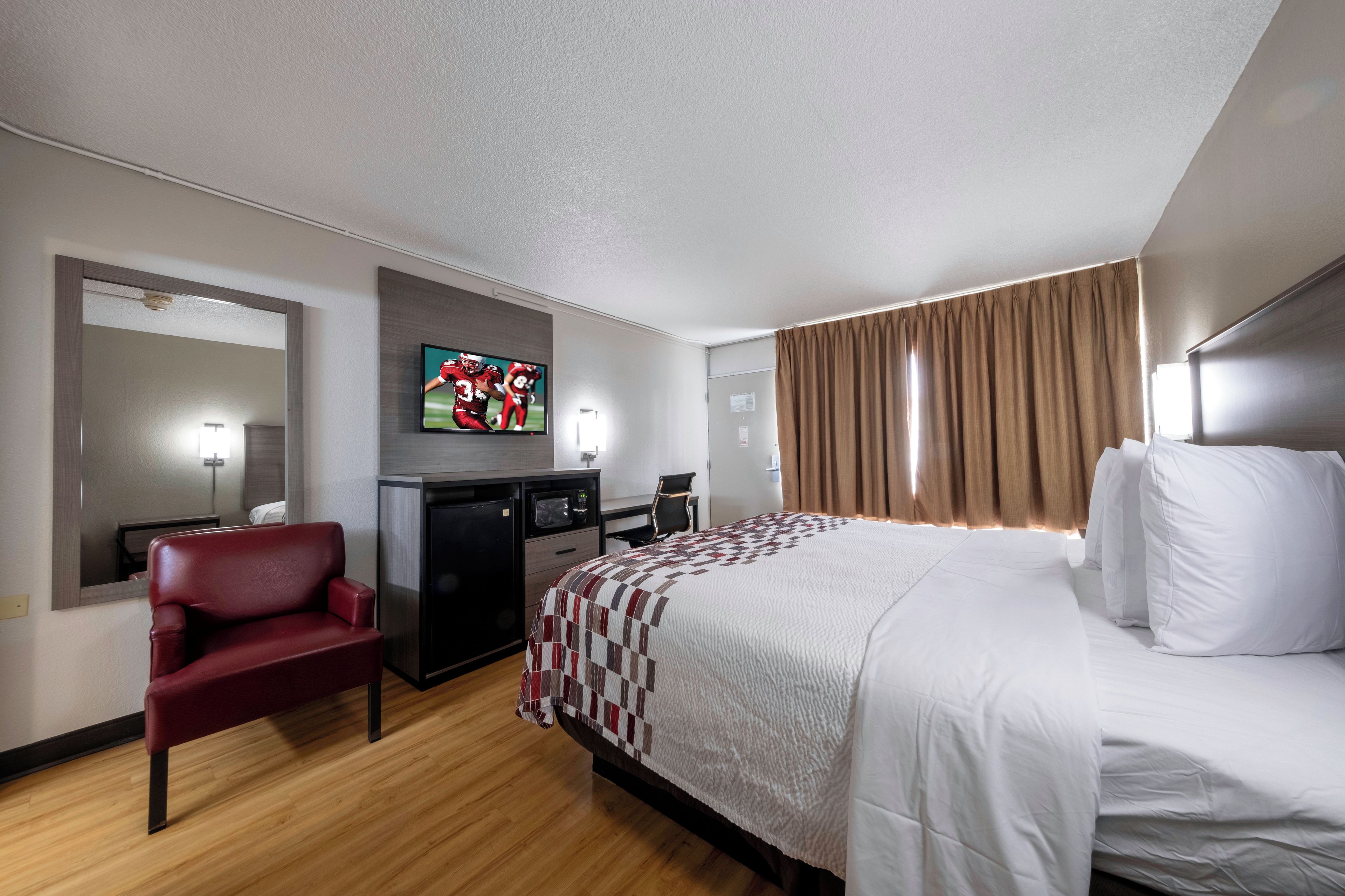 A hotel room with a bed, a desk, a chair, a television, and a mirror.