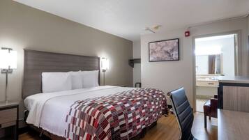 Habitación de hotel con cama, lámparas de noche, un escritorio con silla, un cuadro en la pared y una ventana.