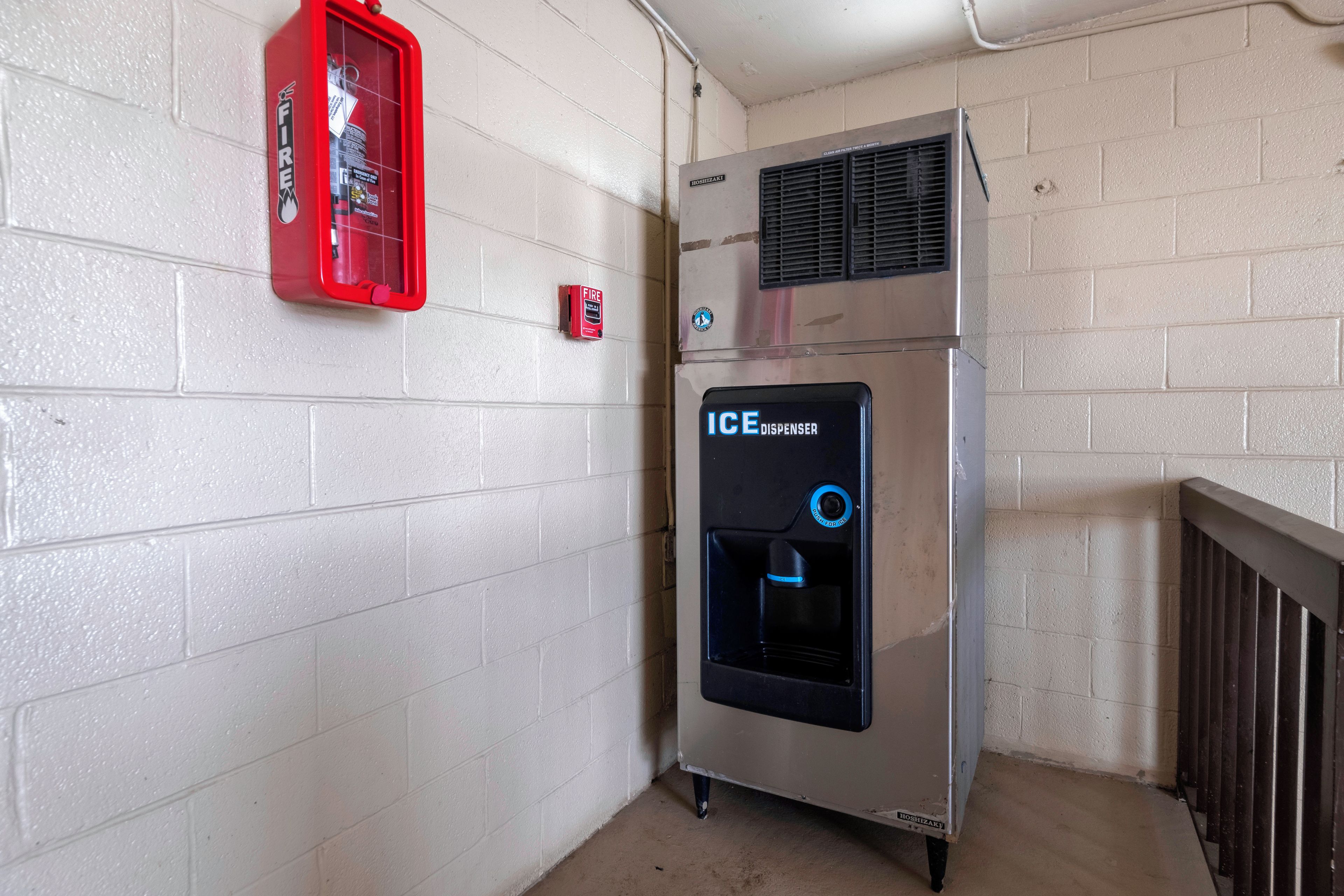 Una máquina expendedora con dispensador de hielo, extintor y termostato instalado en la pared.