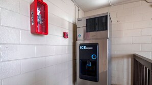 Ein Getränkeautomat mit Eisspender, einem Feuerlöscher und einem an der Wand montierten Thermostat.