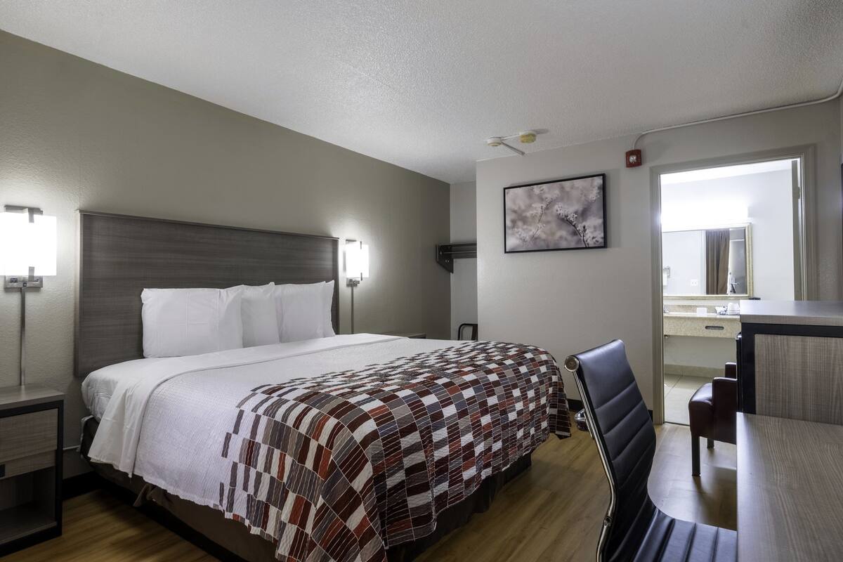 A hotel room with a bed, bedside tables, a desk, and a chair.