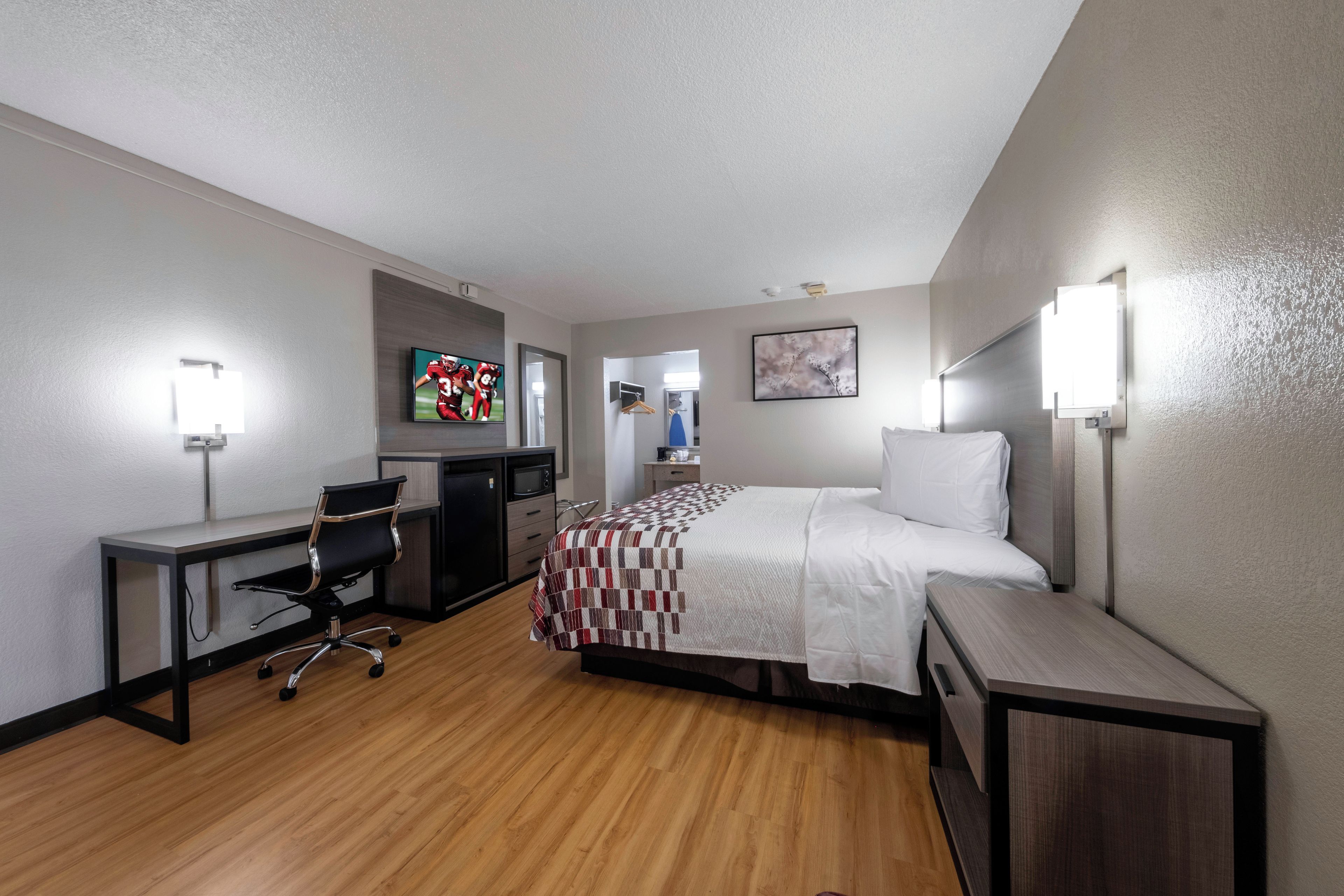 A hotel room with a bed, desk, chair, and a television.