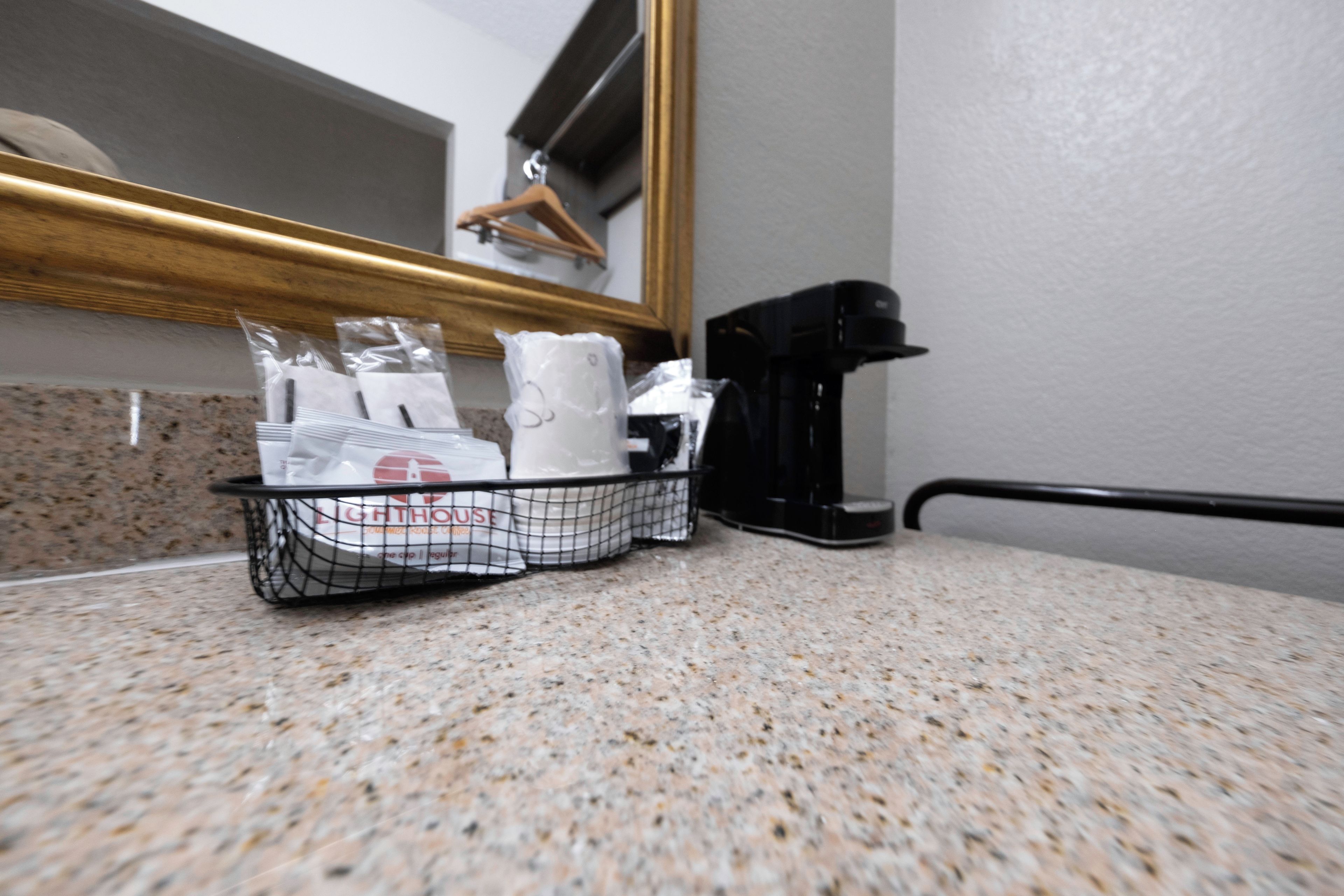 A kitchen counter with a coffee maker, a basket of toiletries, and a hanging towel rack.