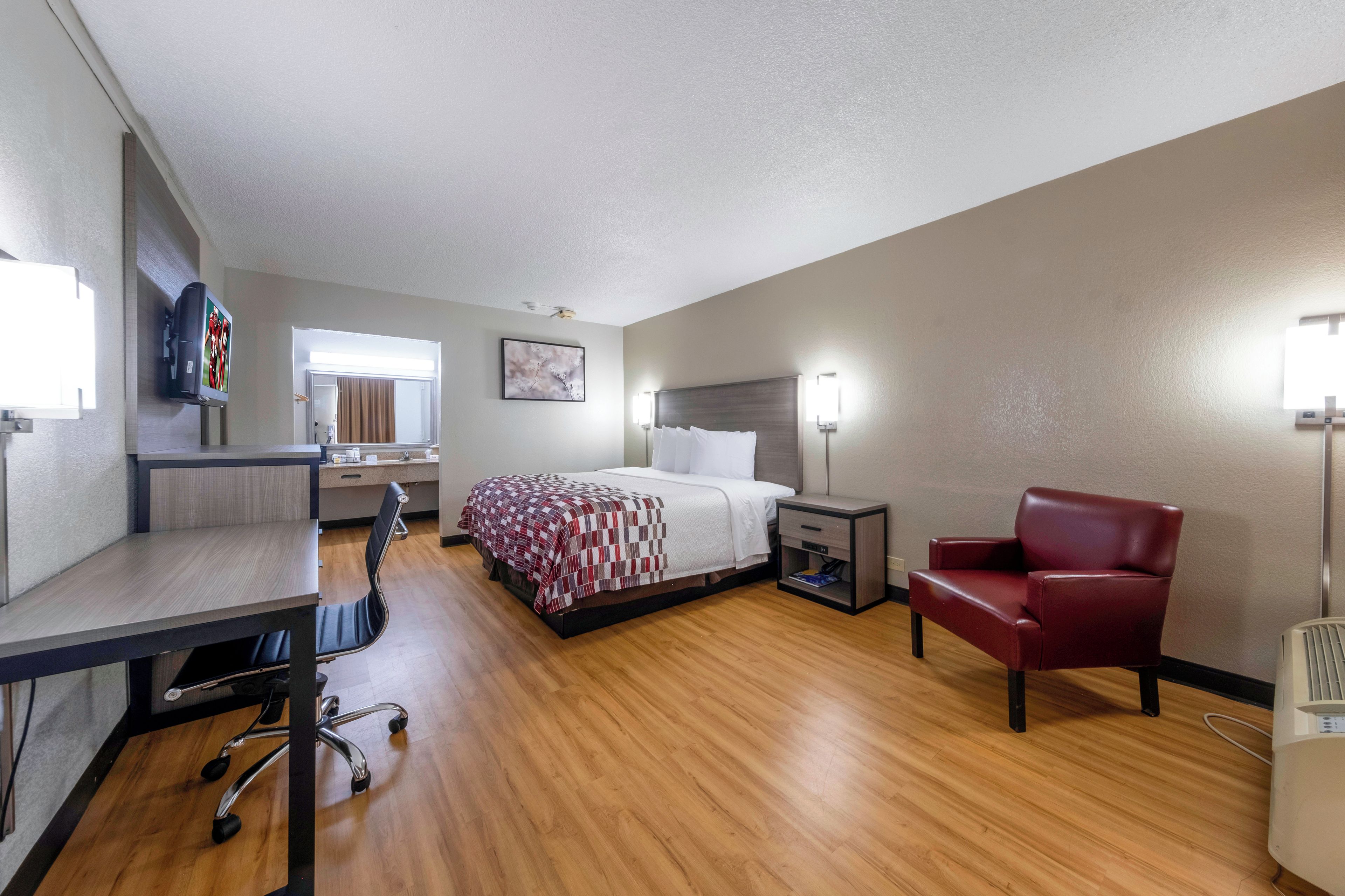 A hotel room with a bed, desk, chair, bedside table, and a television.
