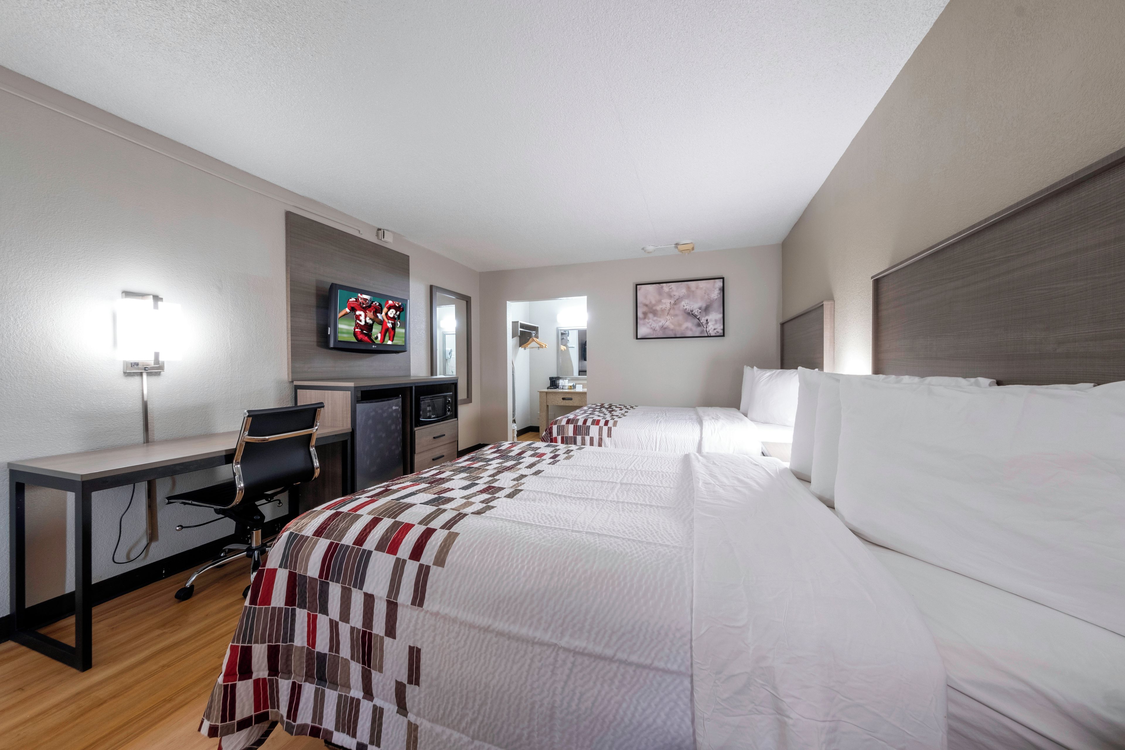 A hotel room with a bed, a desk, a chair, a television, and a painting on the wall.