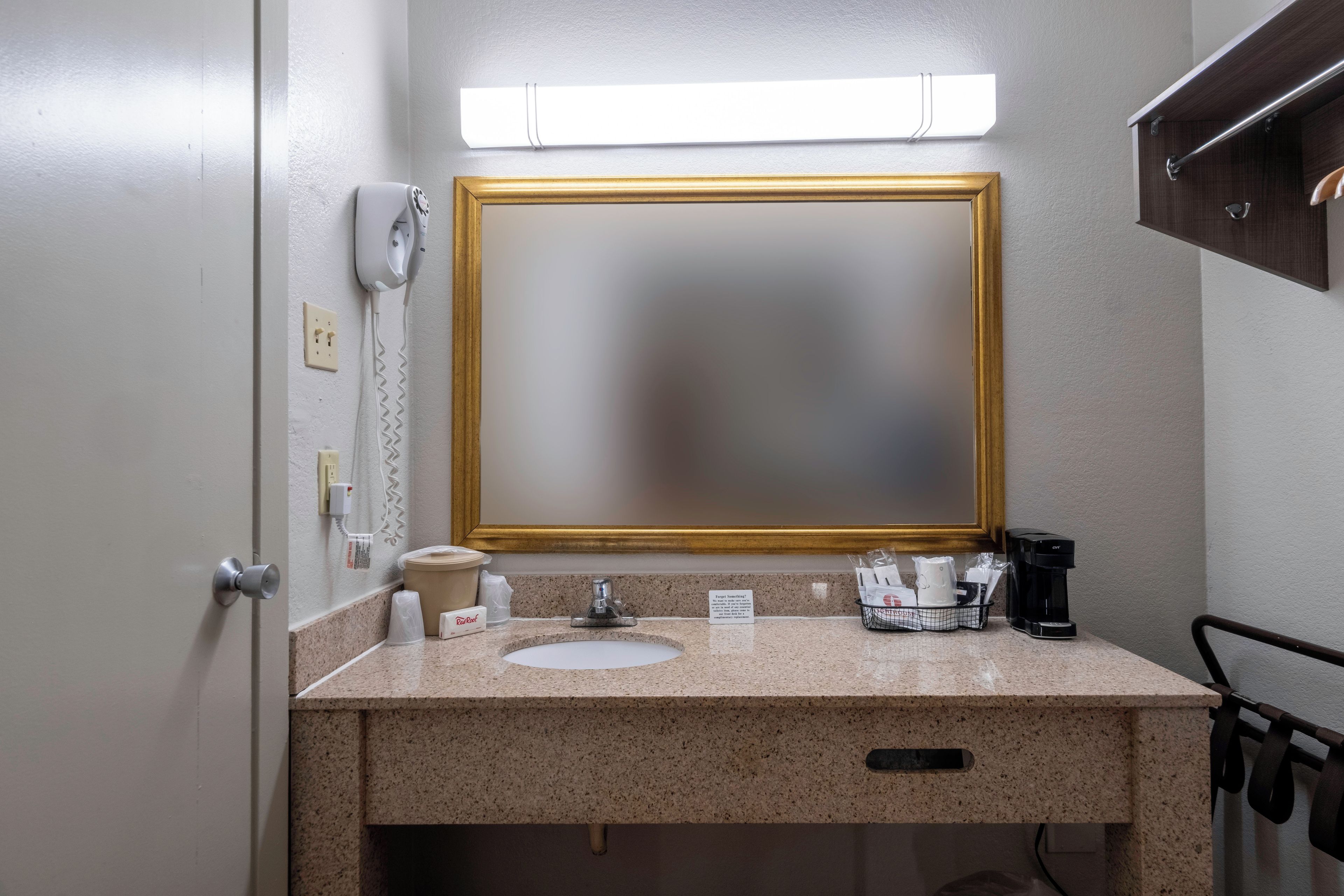 A bathroom with a countertop sink, a mirror, a towel dispenser, and a coffee maker.