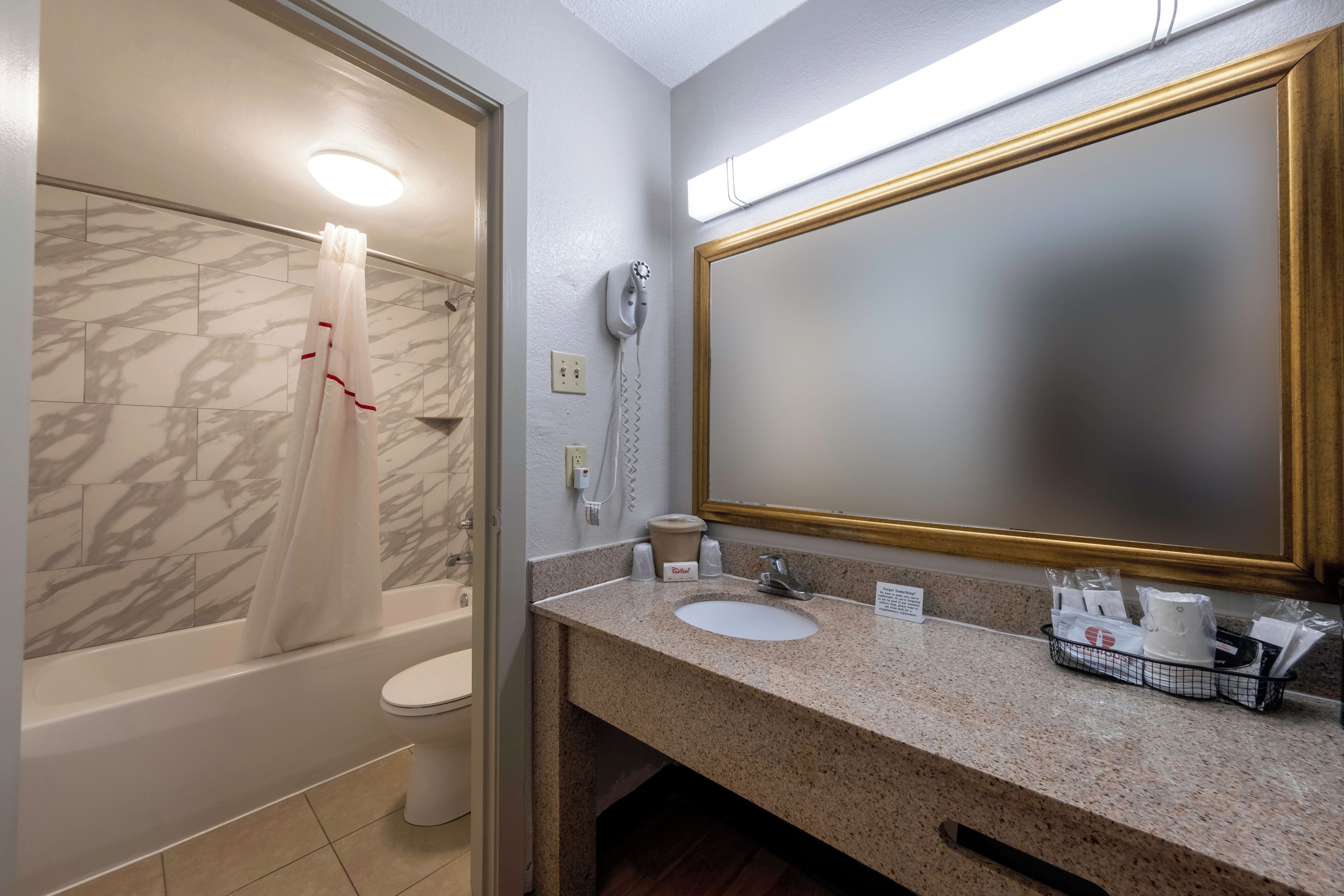 A bathroom with a marble-tiled shower, a toilet, a sink with a granite countertop, and a large mirror with a gold frame.