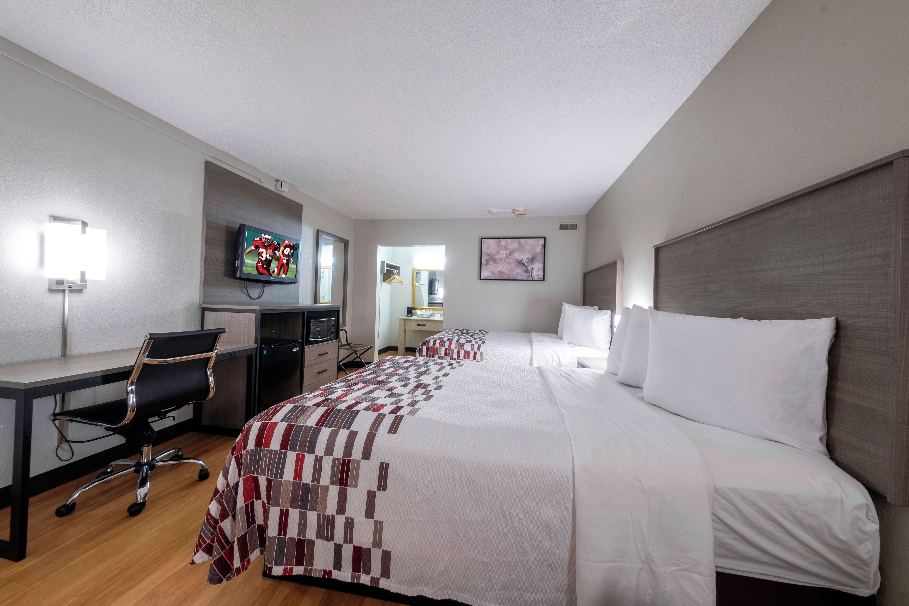A hotel room with a bed, desk, chair, television, and a painting on the wall.