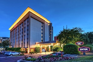 A modern hotel entrance with a 'Welcome' sign, 'Hampton Inn' sign, and an 'Enter' sign.