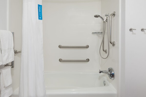 A white bathroom with a bathtub, grab bars, and a shower head.