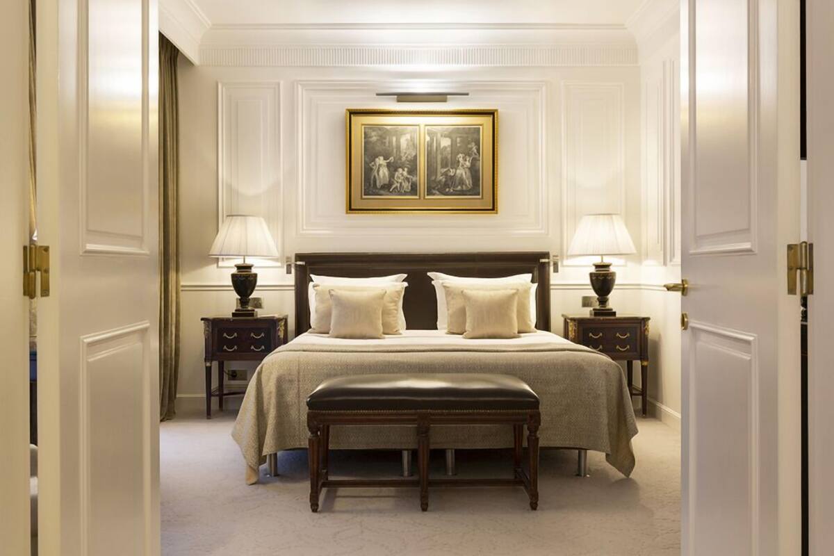 Ein klassisches Hotelzimmer mit einem großen Bett, zwei Nachttischen mit Lampen, einer Bank und einem gerahmten Bild über dem Bett.