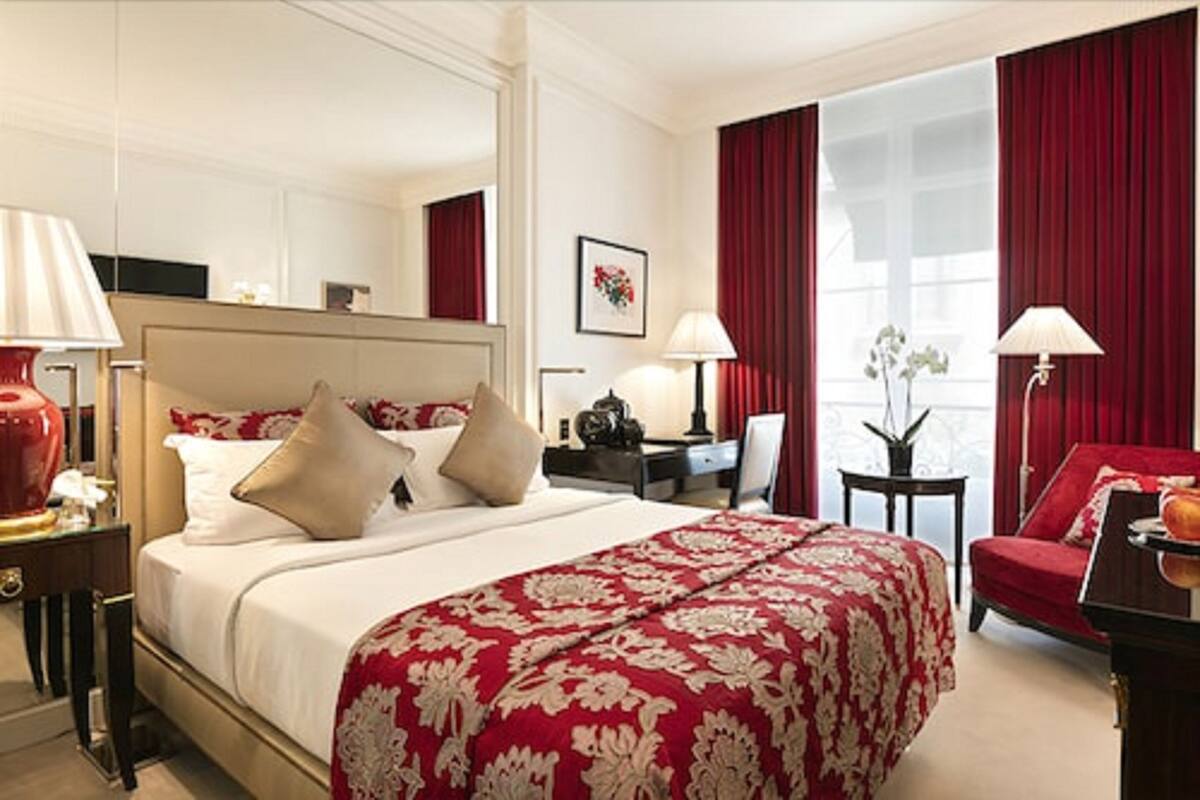 Ein Hotelzimmer mit einem großen Bett, roten Vorhängen, einem Schreibtisch mit Lampe und einem Sessel.