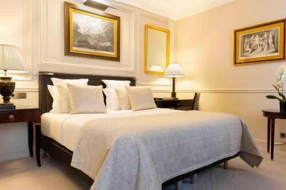Ein Hotelzimmer mit einem großen Bett, zwei Nachttischen, einem Beistelltisch und gerahmten Bildern an den Wänden.