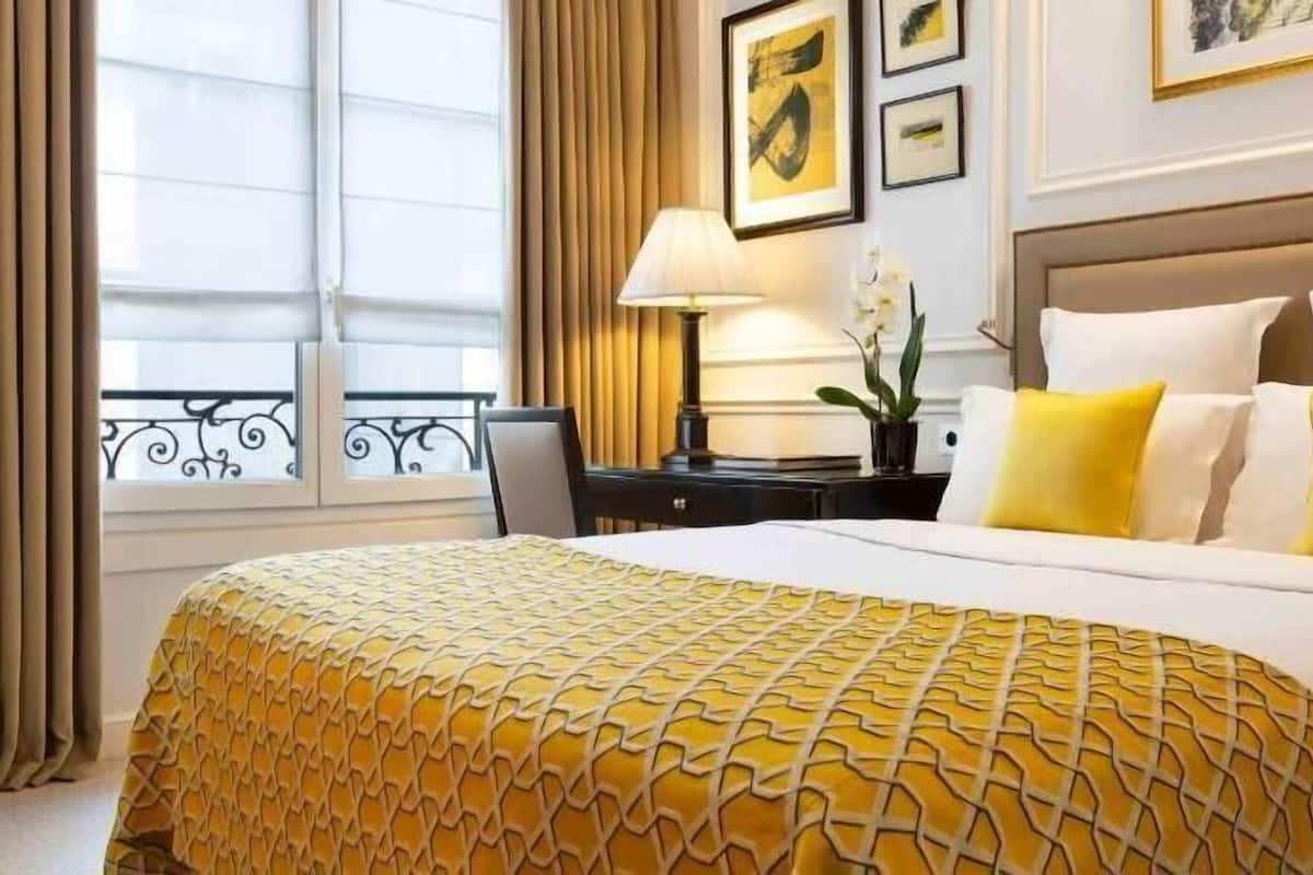 Ein Hotelzimmer mit einem großen Bett, einem Nachttisch, einer Lampe und einem Fenster mit Vorhängen.