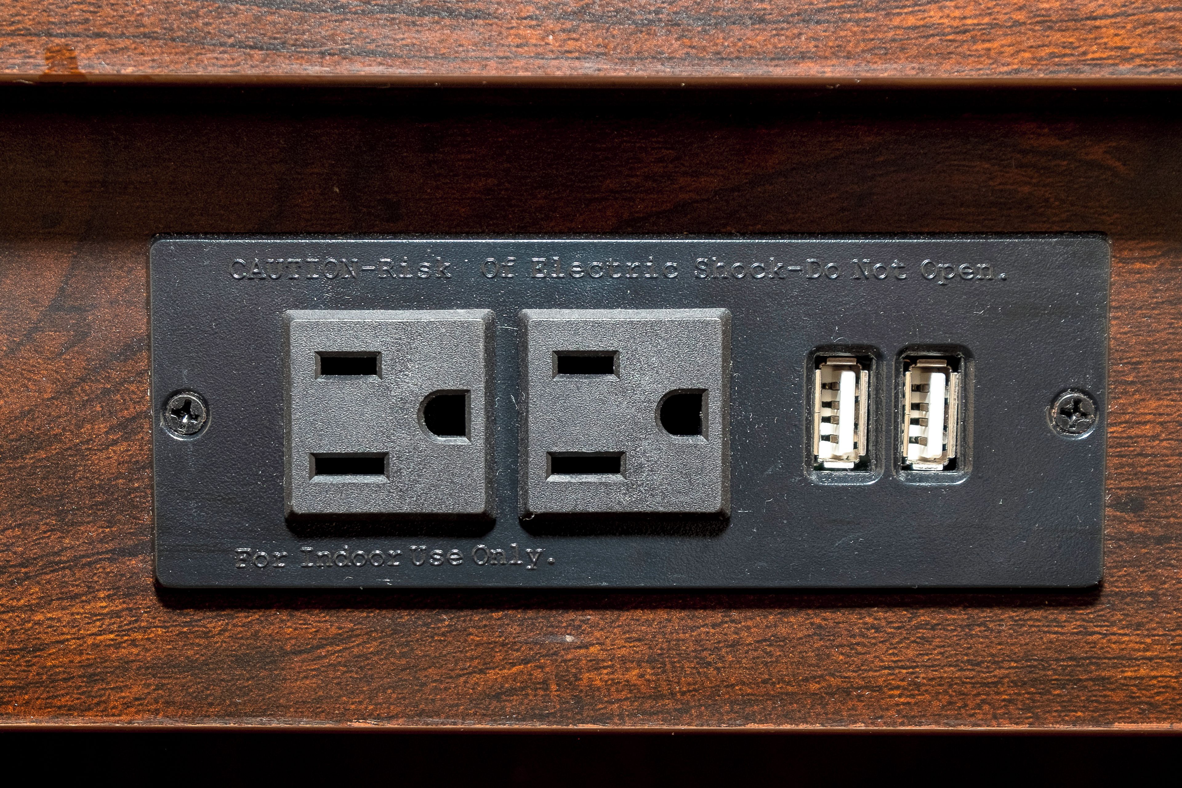 A black electrical outlet with two standard sockets and two USB ports, labeled for indoor use only.