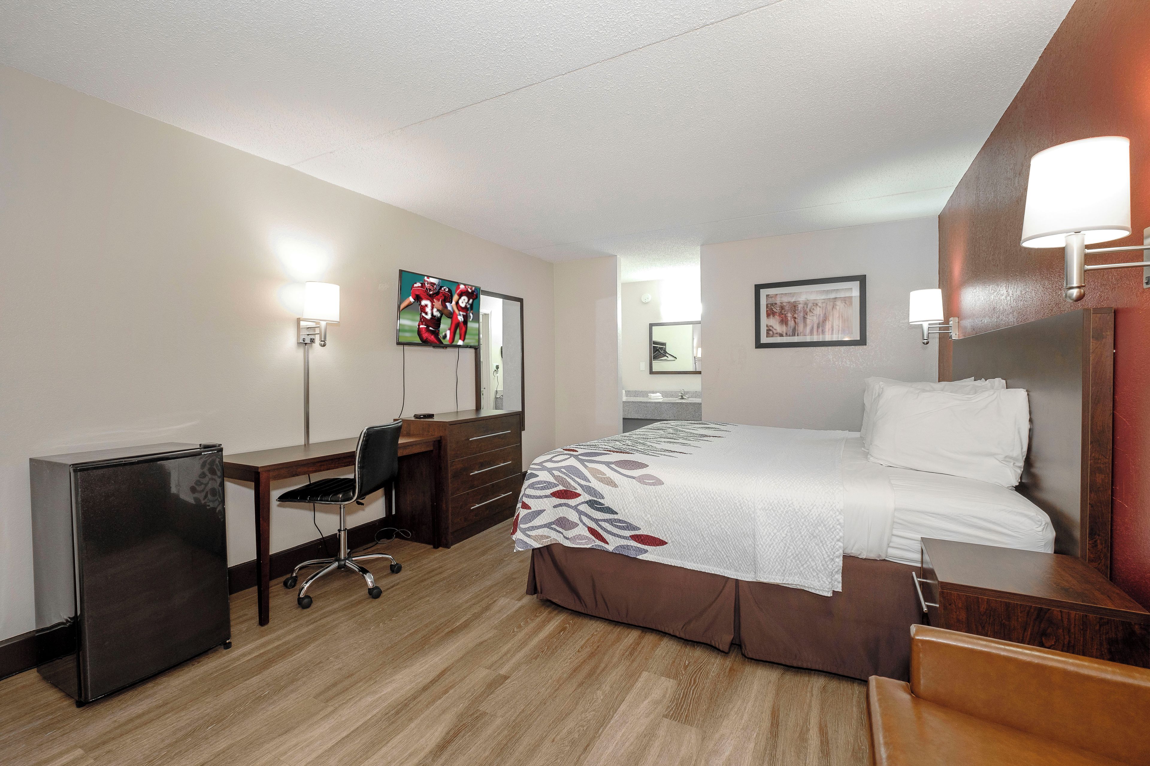 A hotel room with a bed, desk, chair, and a television.