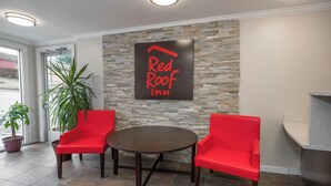 De receptie van een Red Roof Inn met een stenen muur, twee rode stoelen, een ronde tafel en een kamerplant.