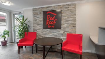 A Red Roof Inn reception area with a stone wall, two red chairs, a round table, and a potted plant.