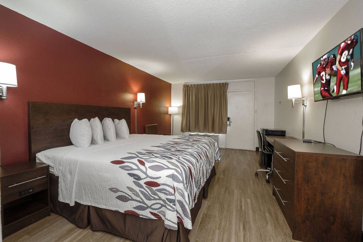 A hotel room with a large bed, bedside tables, a desk, and a TV mounted on the wall.