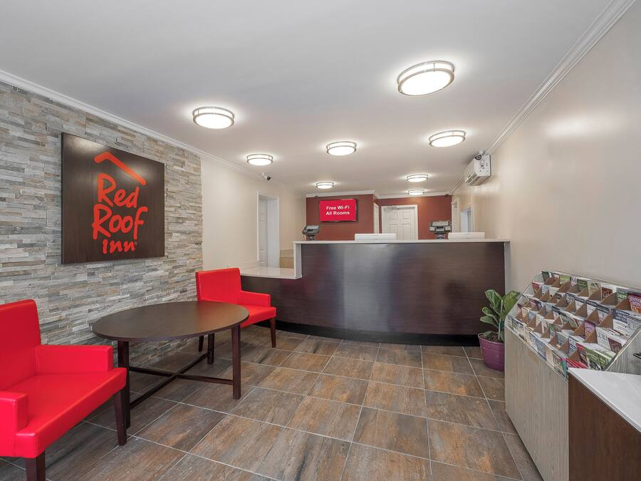 A hotel lobby with a reception desk, a red sofa, a table, and a wall-mounted sign.