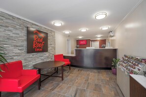 Un vestíbulo de hotel con un mostrador de recepción, un sofá rojo, una mesa y un letrero en la pared.