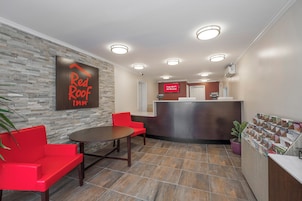 Un hall d’hôtel avec un comptoir d’accueil, un canapé rouge, une table et un panneau fixé au mur.