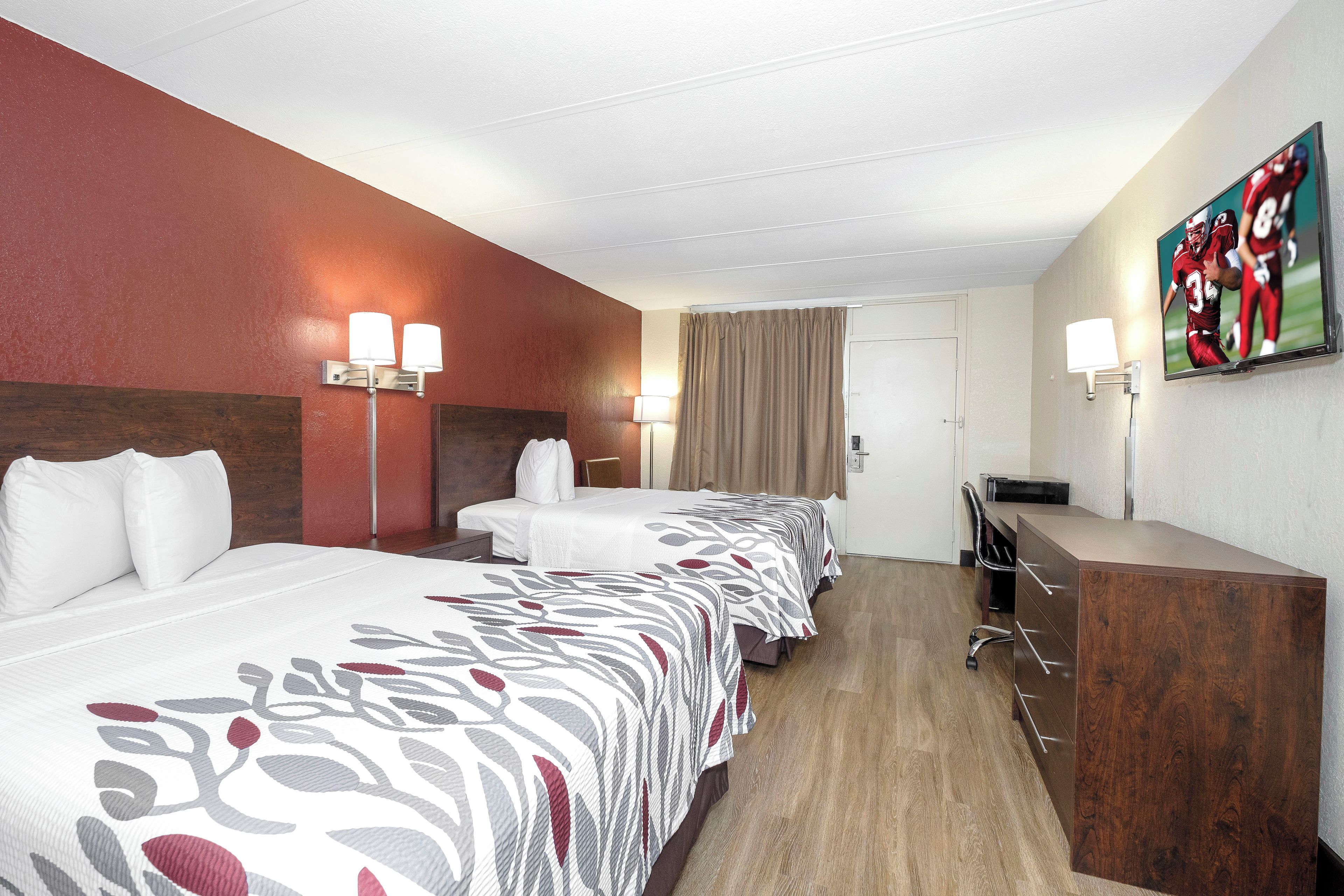 Una habitación de hotel con una cama grande, un escritorio, una silla, un televisor y un cuadro en la pared.