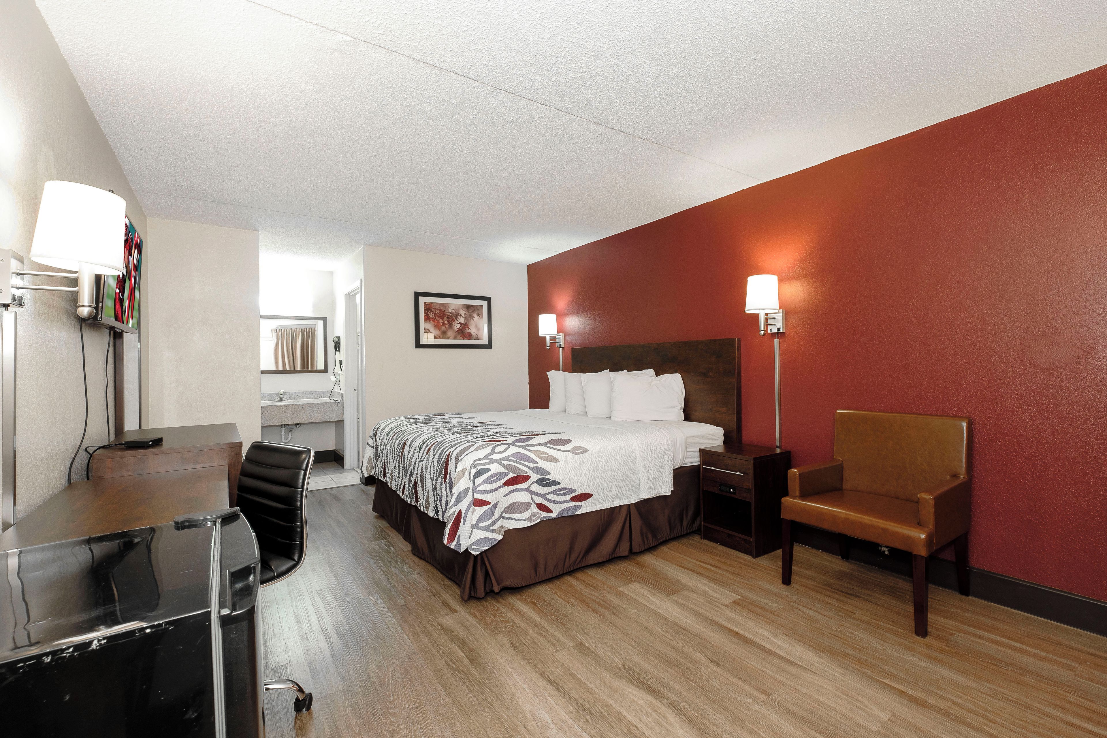 Una habitación de hotel con cama, escritorio, silla, mesita de noche y lámpara.