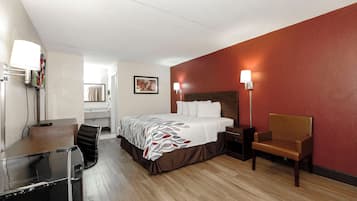 Una habitación de hotel con cama, escritorio, silla, mesita de noche y lámpara.