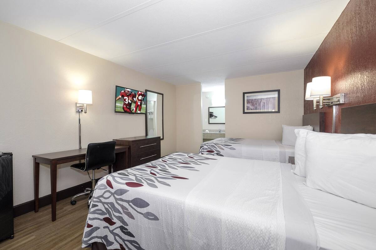 Una habitación de hotel con dos camas, un escritorio, una silla y una lámpara de escritorio.