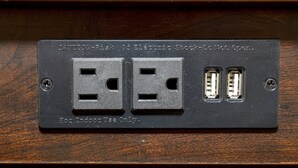 Un enchufe empotrado en la pared con dos tomas de corriente y dos puertos USB, etiquetado para uso exclusivo en interiores.