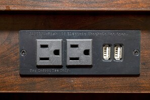 Un enchufe empotrado en la pared con dos tomas de corriente y dos puertos USB, etiquetado para uso exclusivo en interiores.